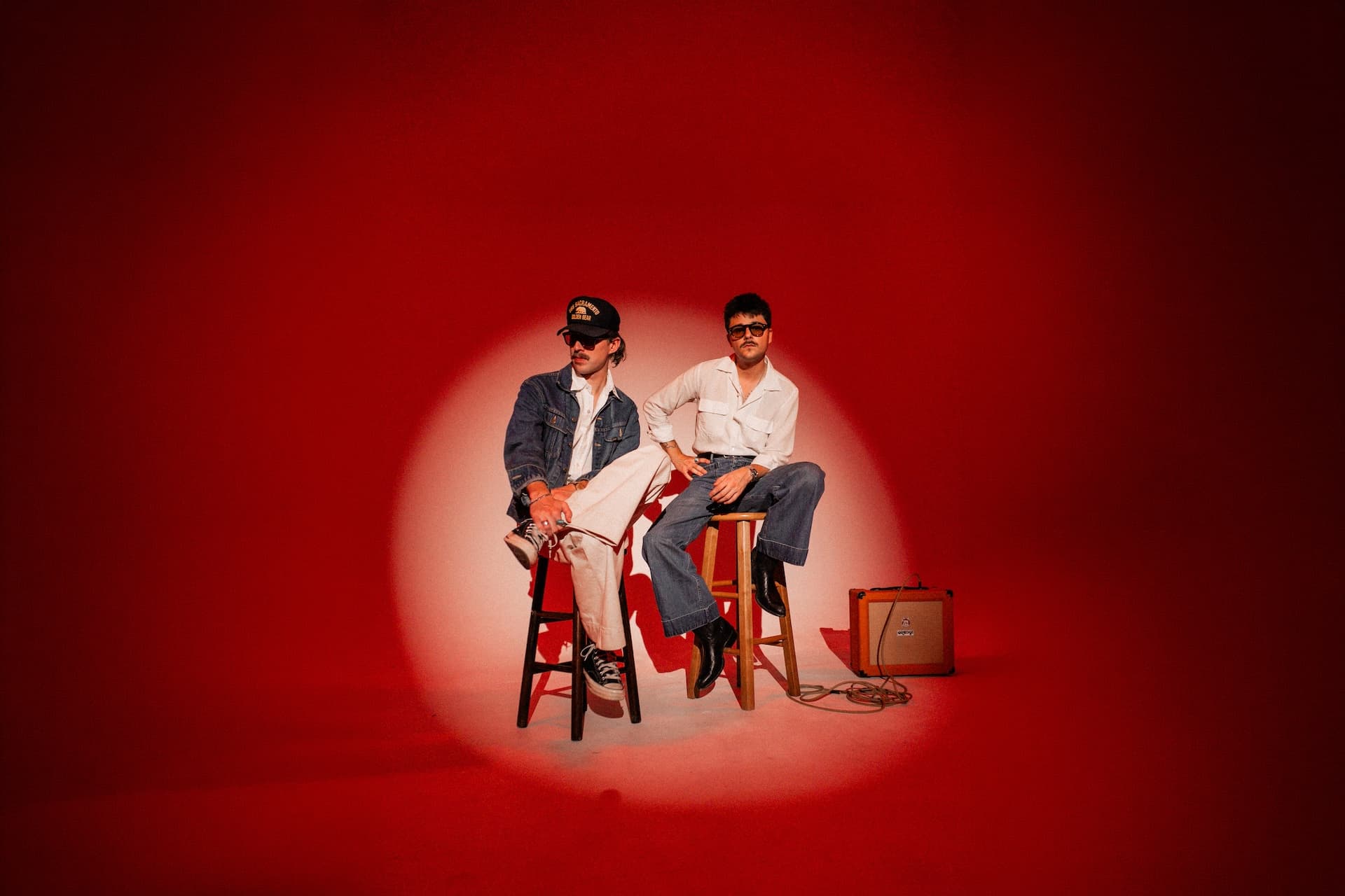 Marfa band members seated on stools under a spotlight against a red backdrop